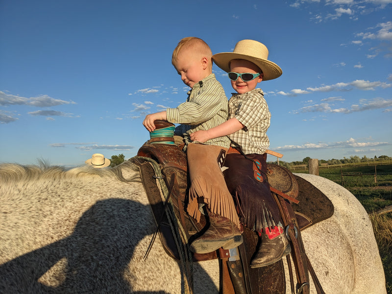 Two children on horseback wearing children's sized custom square leg leather chinks with a straight fringe.